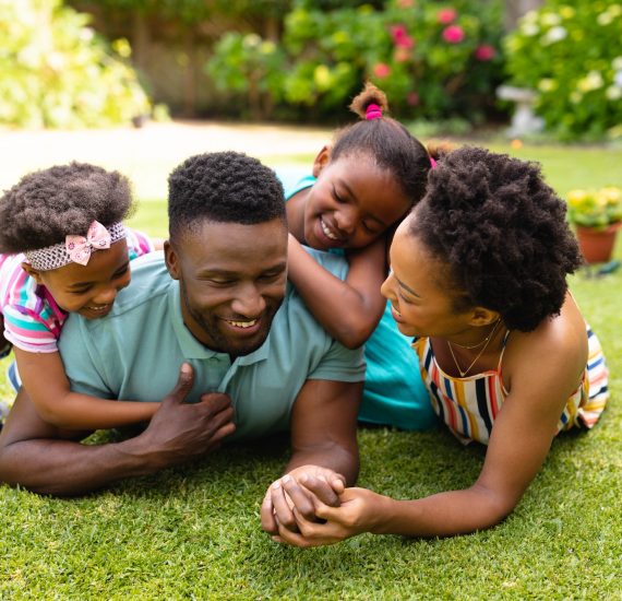 Happy african american family lying on grass at backyard garden